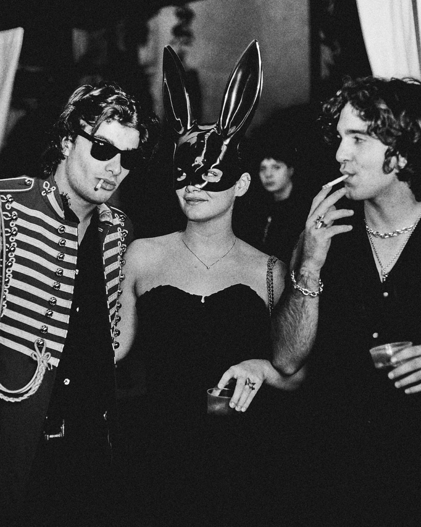 Black and white portrait of three guests posing at the Acido Lattico Magazine x Carnale event, including one person wearing a rabbit mask, photographed by Wilson Ballarin.
